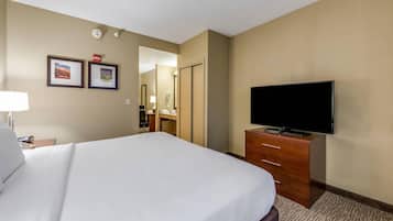 A hotel room with a large bed, a flat-screen TV, a wooden dresser, and a desk with a lamp.