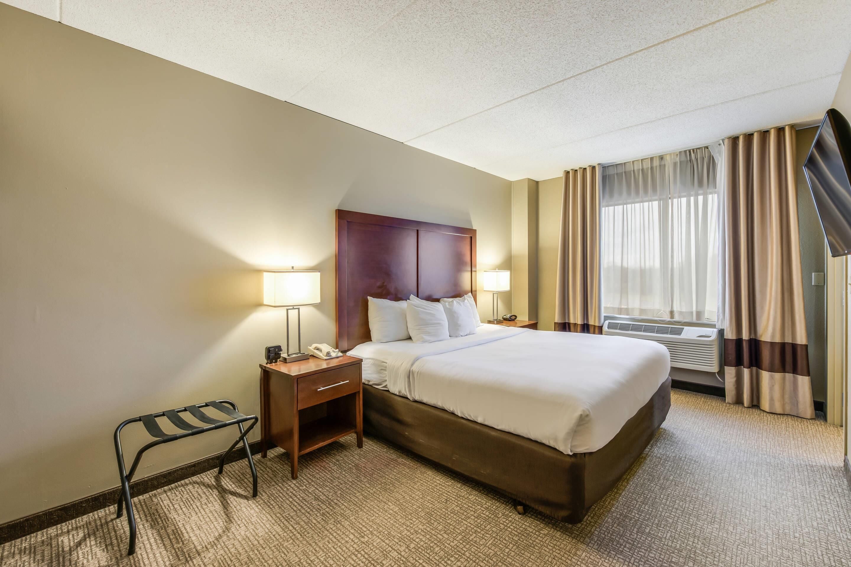 A hotel room with a large bed, two bedside tables with lamps, a small chair, and a window with curtains.
