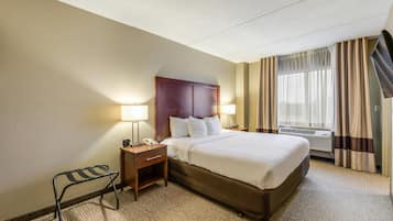 A hotel room with a large bed, two bedside tables with lamps, a small chair, and a window with curtains.