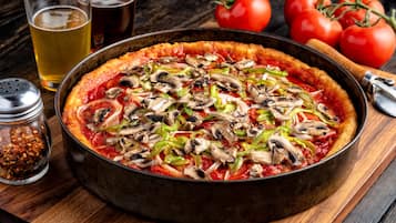 A pizza with toppings, a glass of beer, and tomatoes on a wooden table.