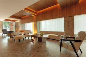 A spacious lobby with a modern design, featuring a large sofa, multiple seating options, and a large window providing natural light.