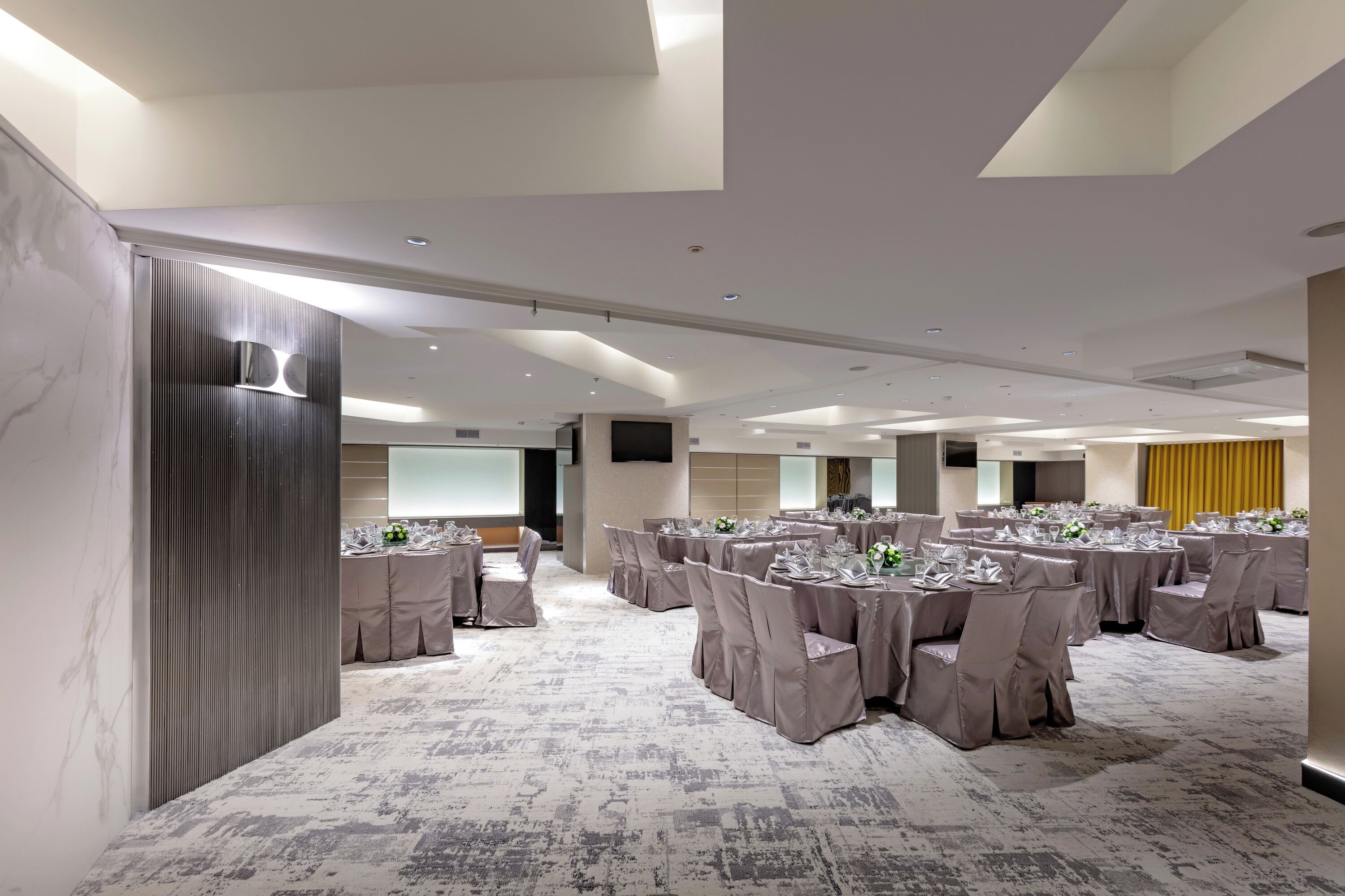 A conference room with multiple round tables, each set with chairs and tablecloths, and a large screen at the front.