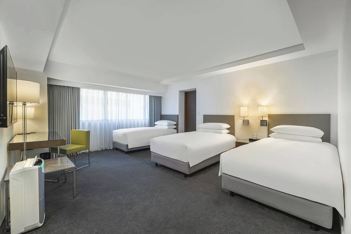 A hotel room with two beds, a desk, a chair, a TV, and a window with curtains.