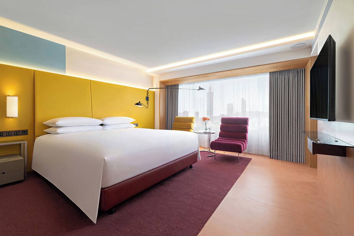 A hotel room with a large bed, a desk, a chair, a TV, and a window with curtains.