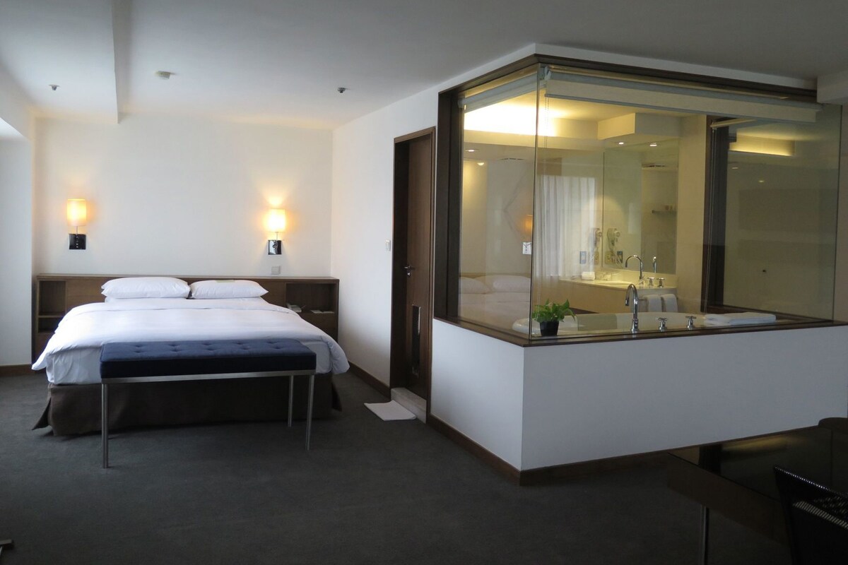 A modern hotel room with a bed, bedside lamps, a large mirror, and a small plant.
