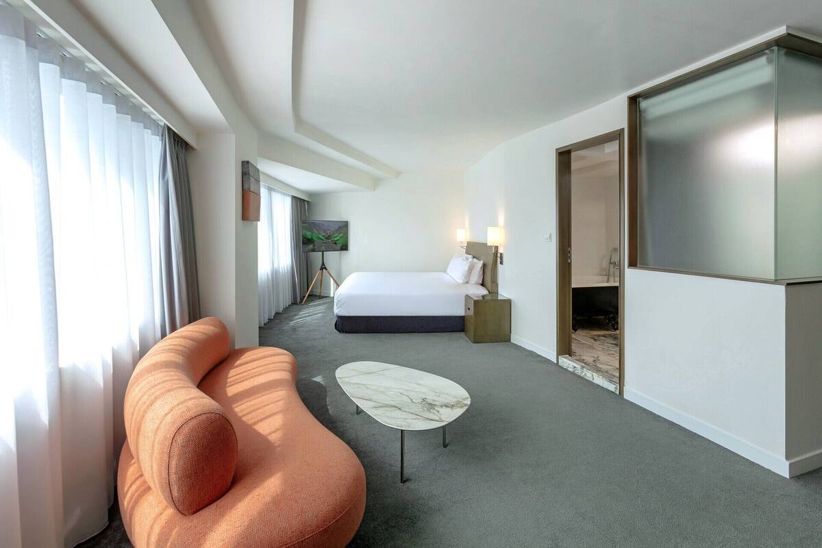 A hotel room with a bed, a sofa, a small table, a TV, and a bathroom.