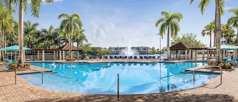 A swimming pool with a fountain, surrounded by palm trees and lounge chairs.