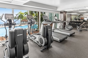 A gym with treadmills, ellipticals, and dumbbells, overlooking a pool with palm trees. - Marriott's Villas at Doral (Miami)