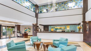 Un hall d’entrée spacieux, agrémenté de fauteuils turquoise, d’un comptoir de réception et d’un grand lustre.