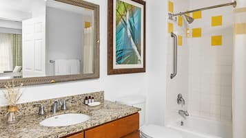 Un baño con lavamanos de granito, inodoro blanco, bañera y ducha con barra de apoyo.