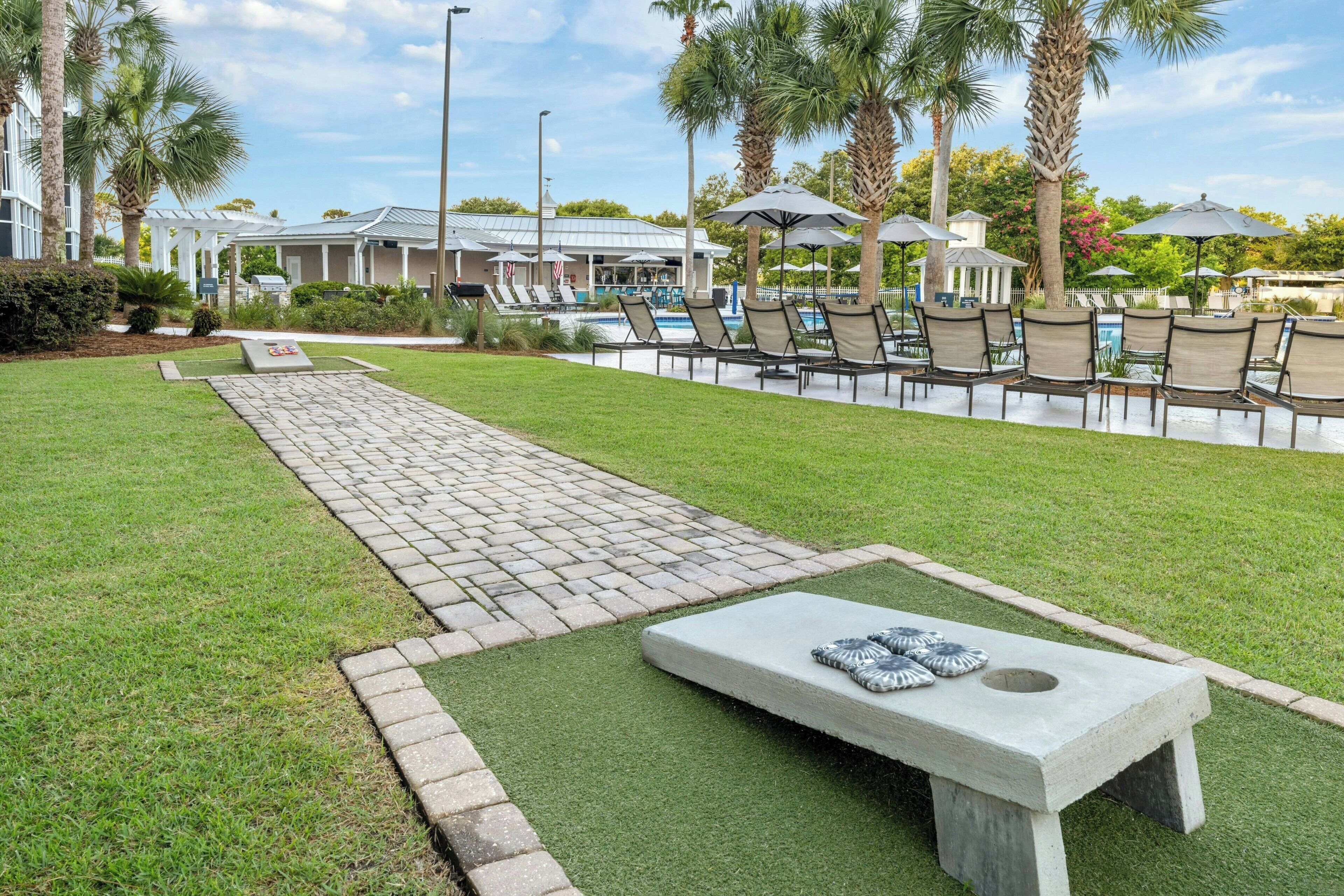 A poolside area with lounge chairs and umbrellas, a concrete bench, and a paved walkway.