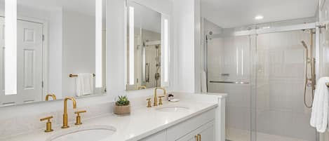 Un baño moderno con lavamanos doble, espejos grandes y ducha con cerramiento de vidrio.