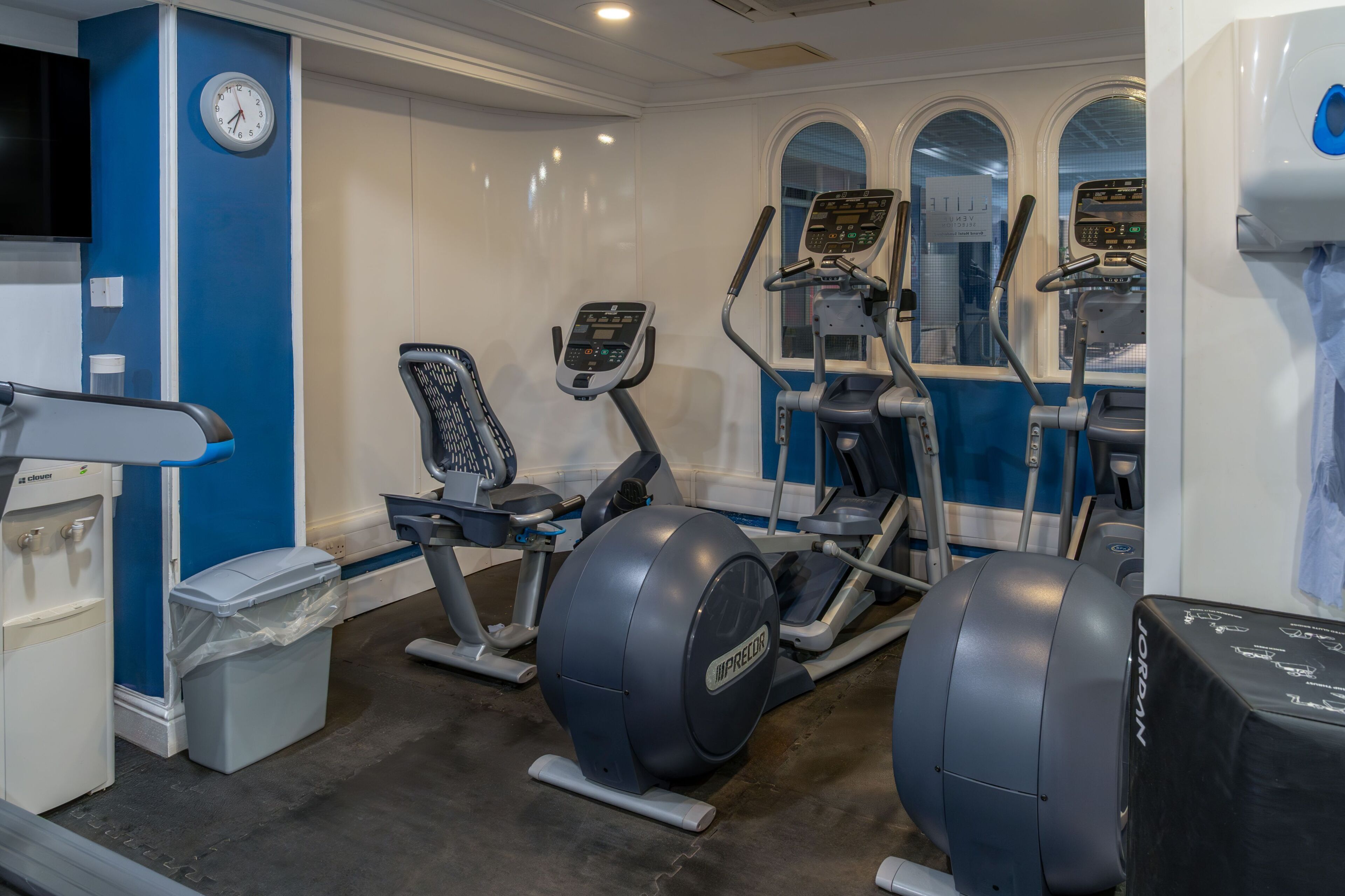 A gym with exercise equipment, a clock, and a trash bin.