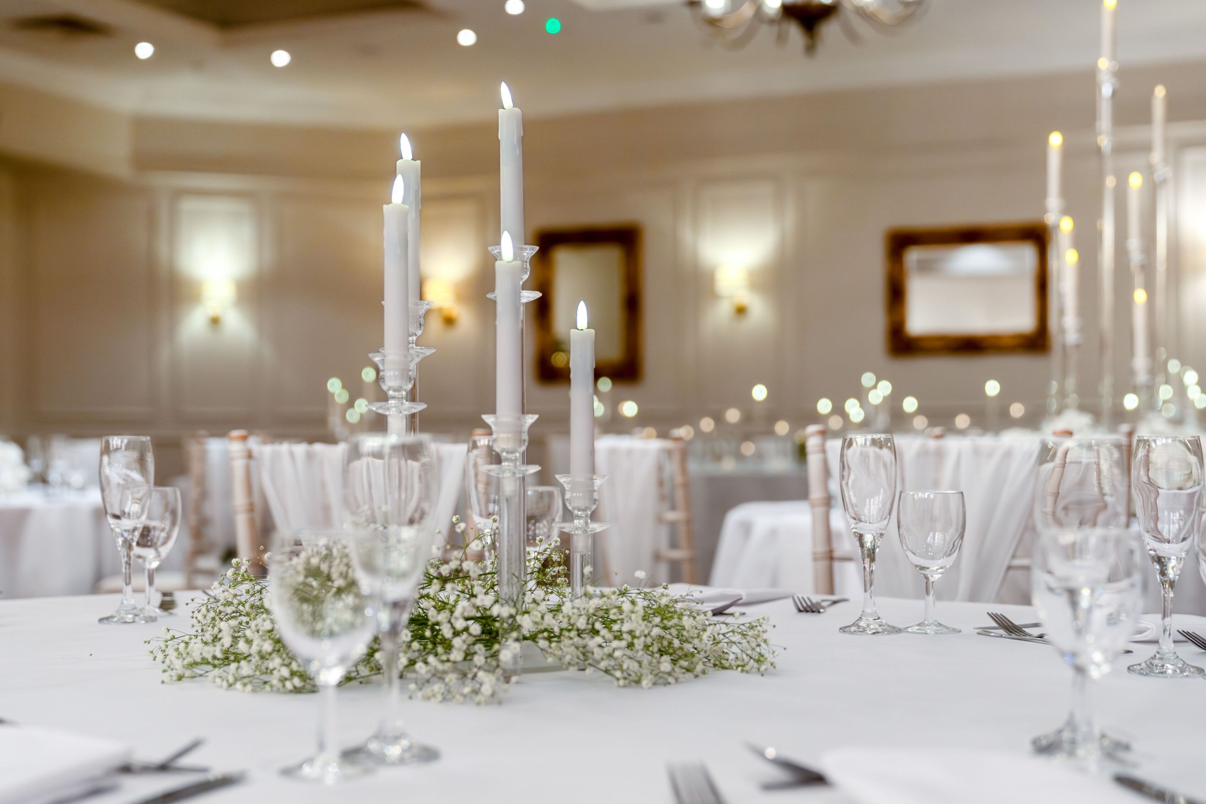 Una mesa con manteles blancos, copas de cristal transparentes y velas blancas altas.