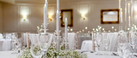 Una mesa con manteles blancos, copas de cristal transparentes y velas blancas altas.