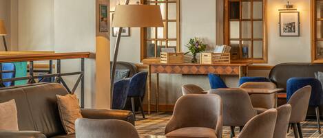 A hotel lobby with a reception desk, seating area with chairs and sofas, and large windows with wooden frames.