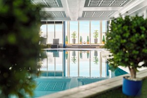 Una piscina interior con reflejos claros, ventanas amplias y plantas en macetas.