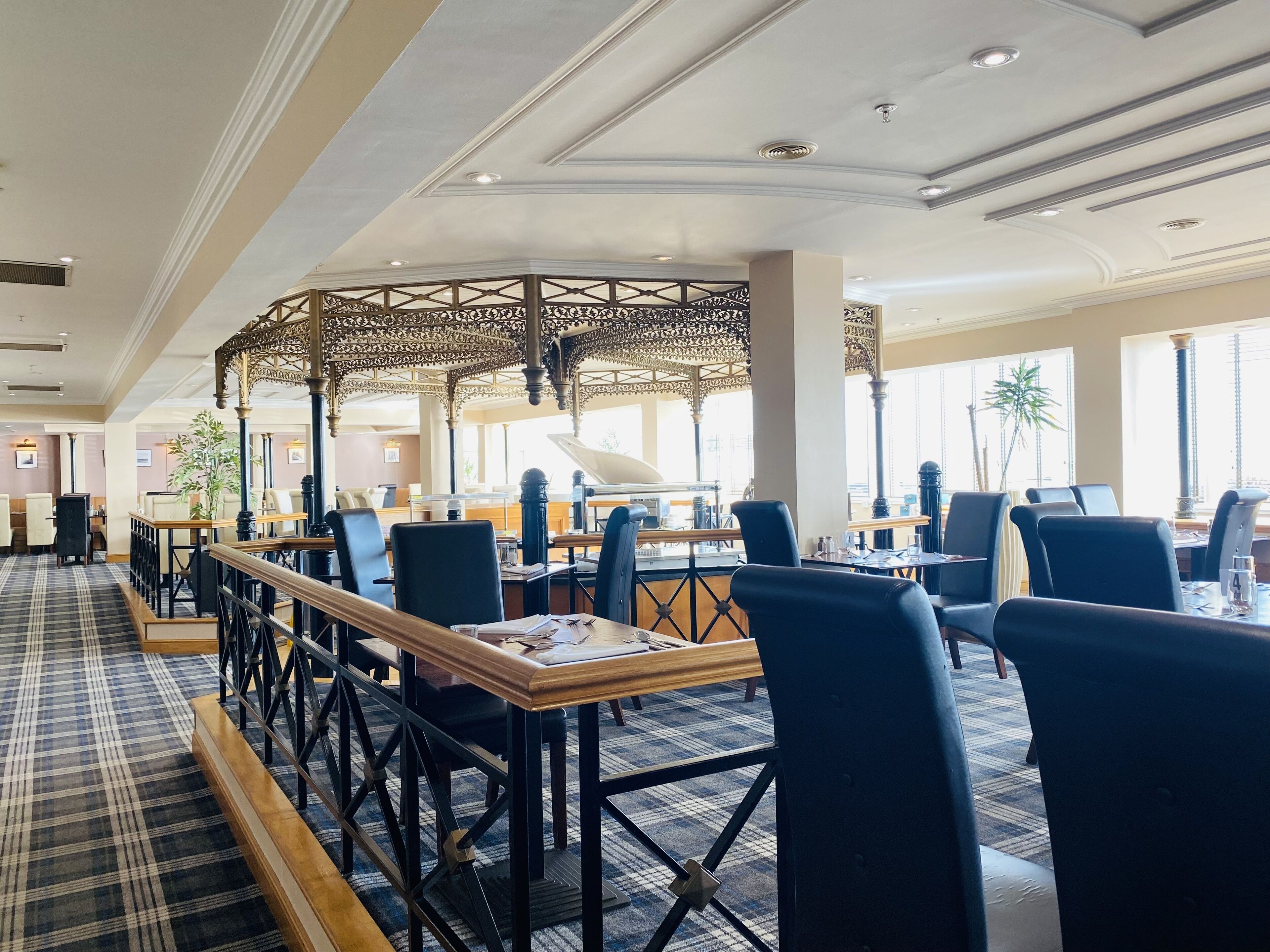 Um restaurante com chão xadrez, cadeiras pretas e uma estrutura decorativa central.