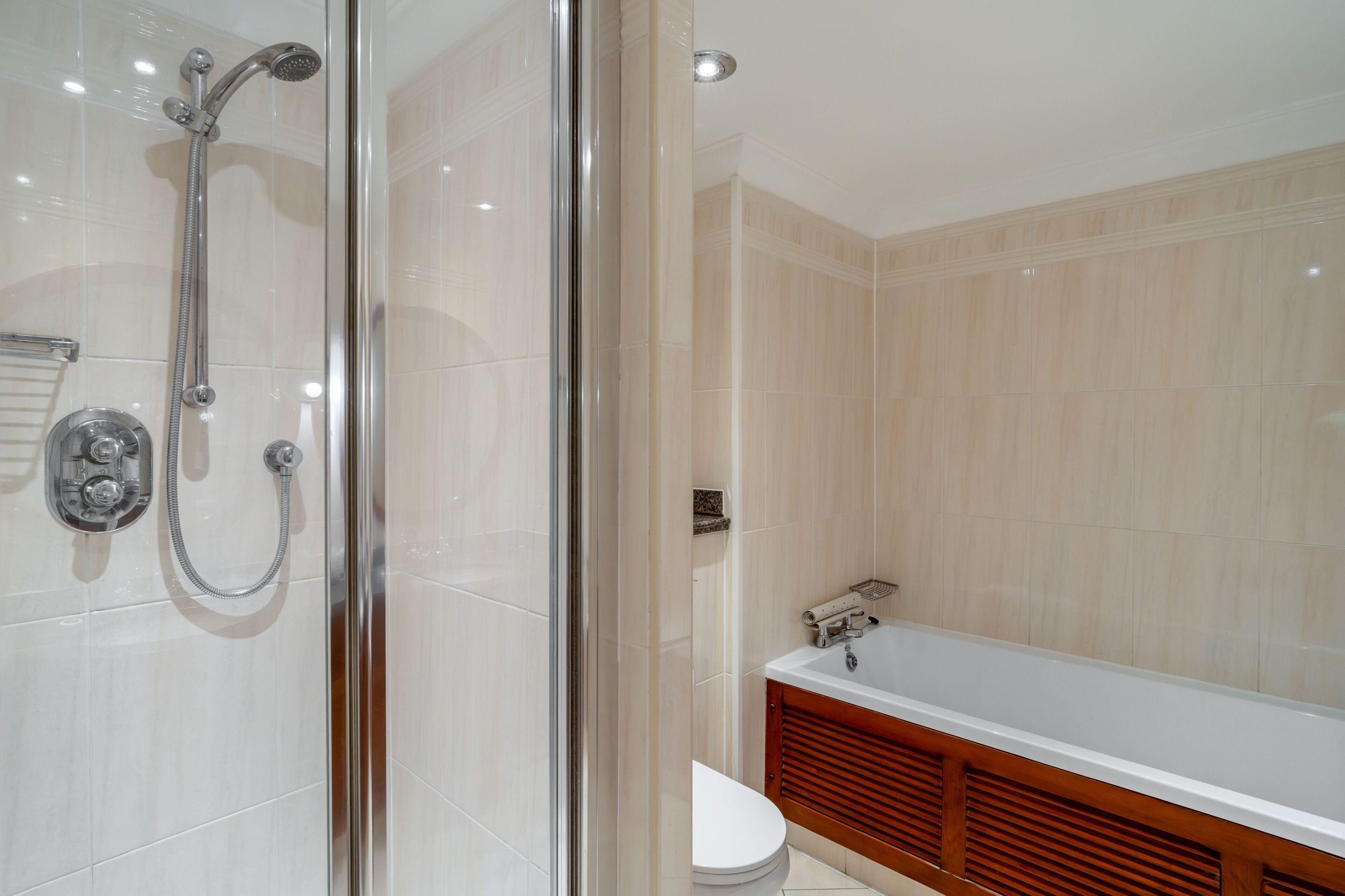 A modern bathroom with a glass shower enclosure, a white toilet, and a wooden vanity with a bathtub.