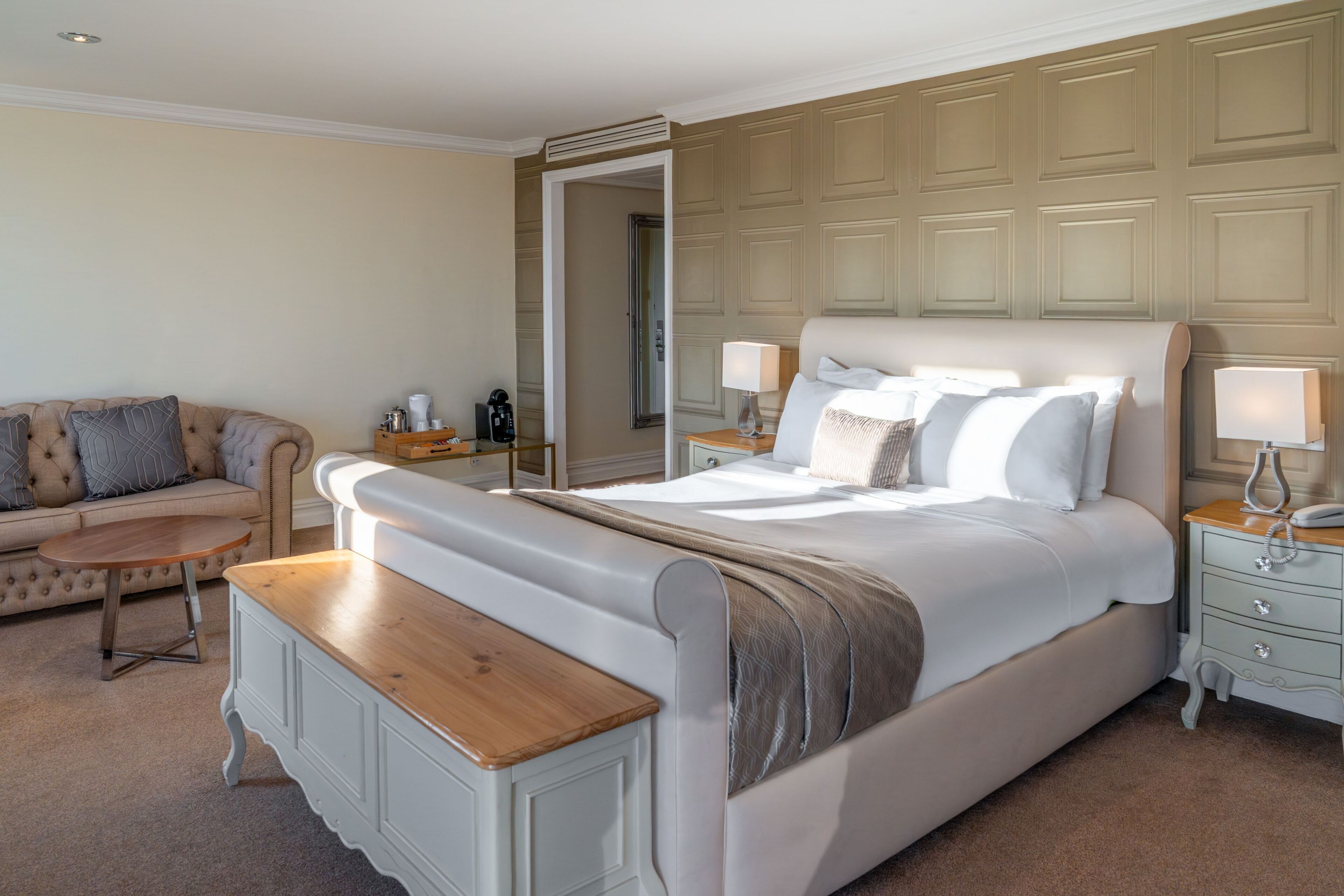 A bedroom with a large bed, bedside tables, a sofa, and a mirror.