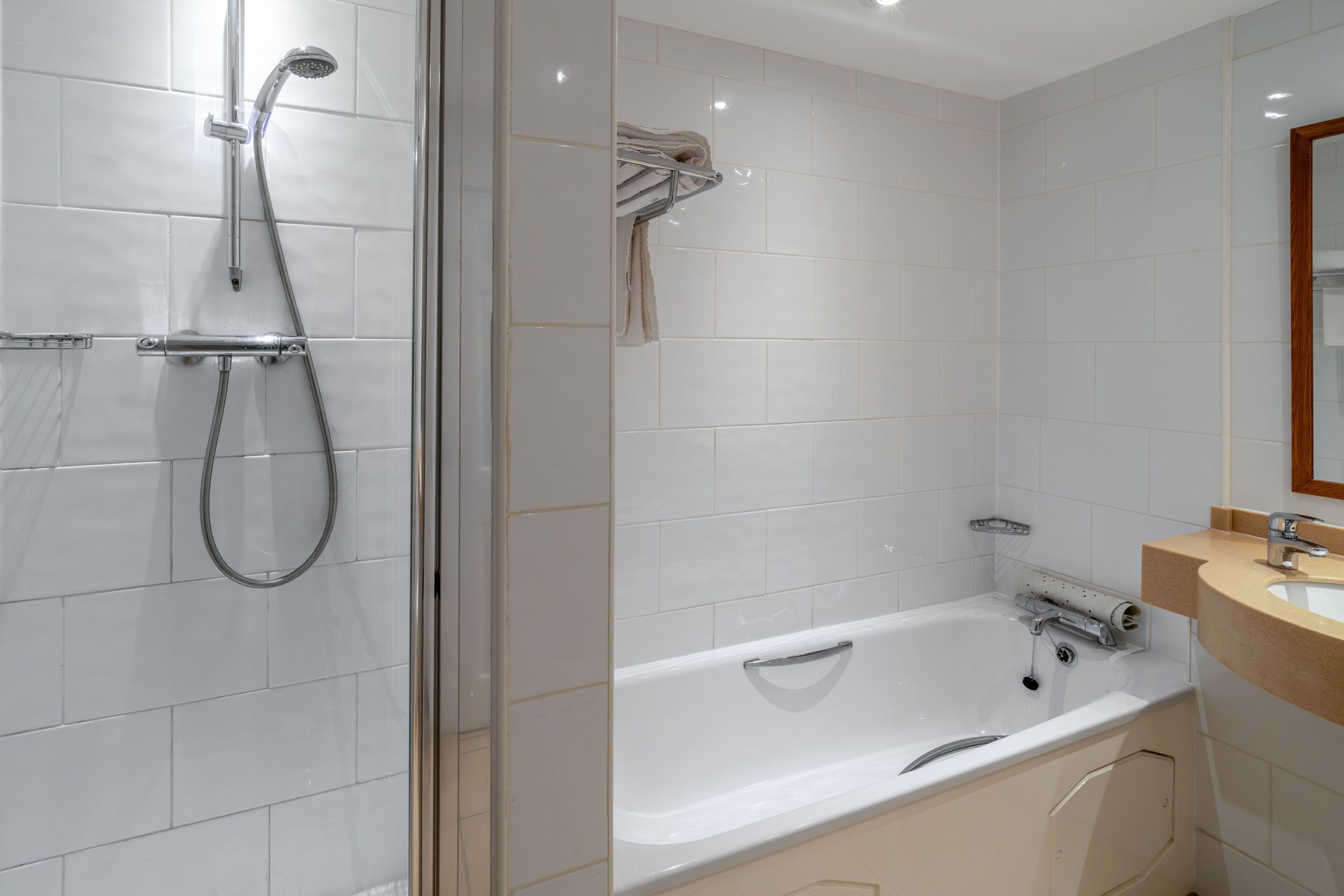 A modern bathroom with a glass-enclosed shower, a white bathtub, and a wooden vanity with a sink.