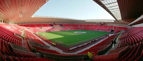 A stadium with red seating, a green field, and a large roof structure.