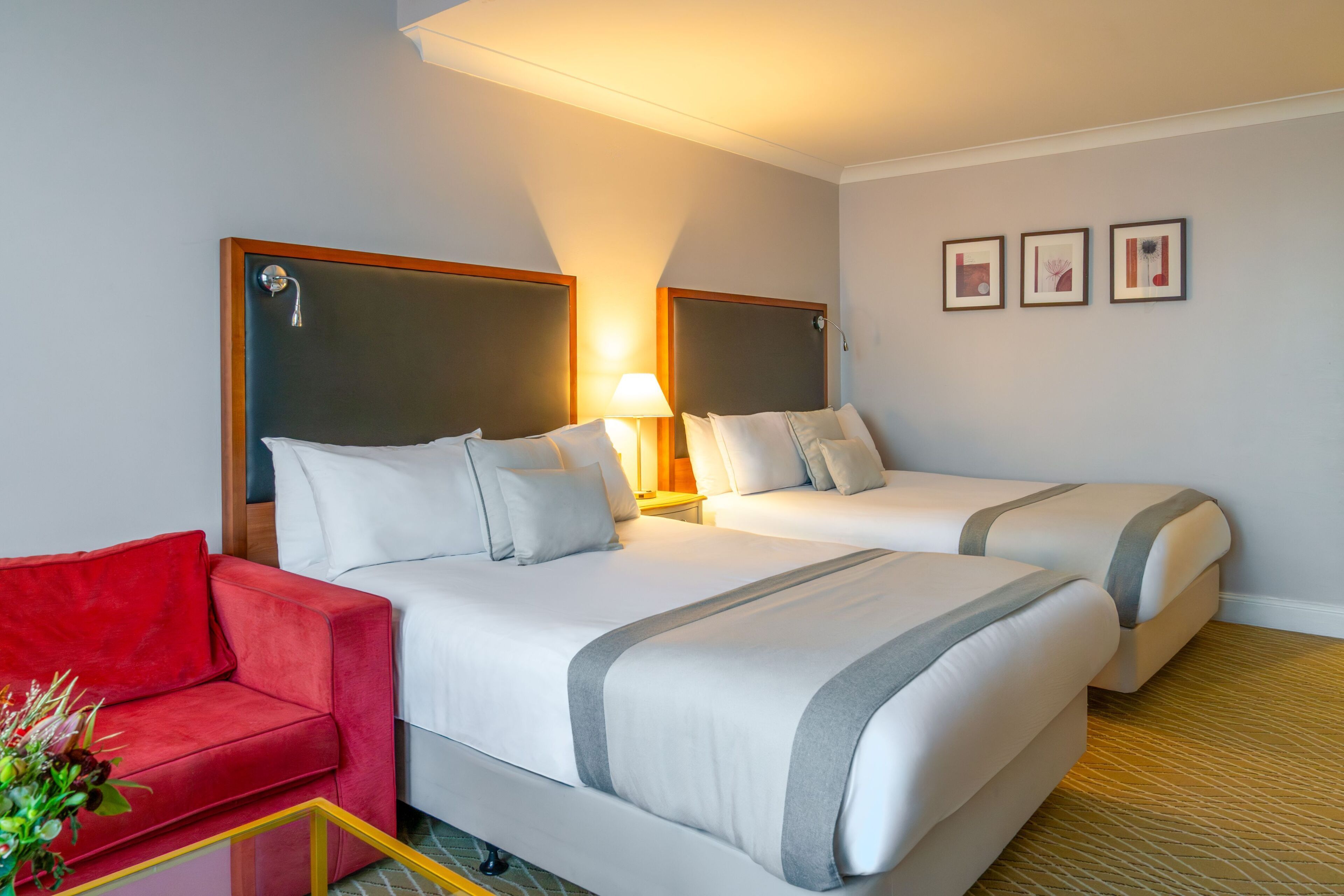 Et hotelværelse med to senge, en rød sofa, en lampe og tre billeder i rammer på væggen.