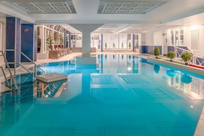 Piscina interior com água cristalina, chão de azulejos e design arquitetônico moderno com paredes azuis e brancas.