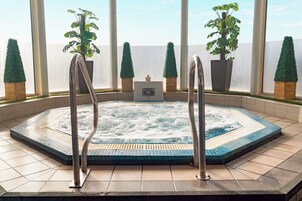 Un jacuzzi con escaleras metálicas, rodeado de plantas en macetas, y vista del cielo a través de amplios ventanales.