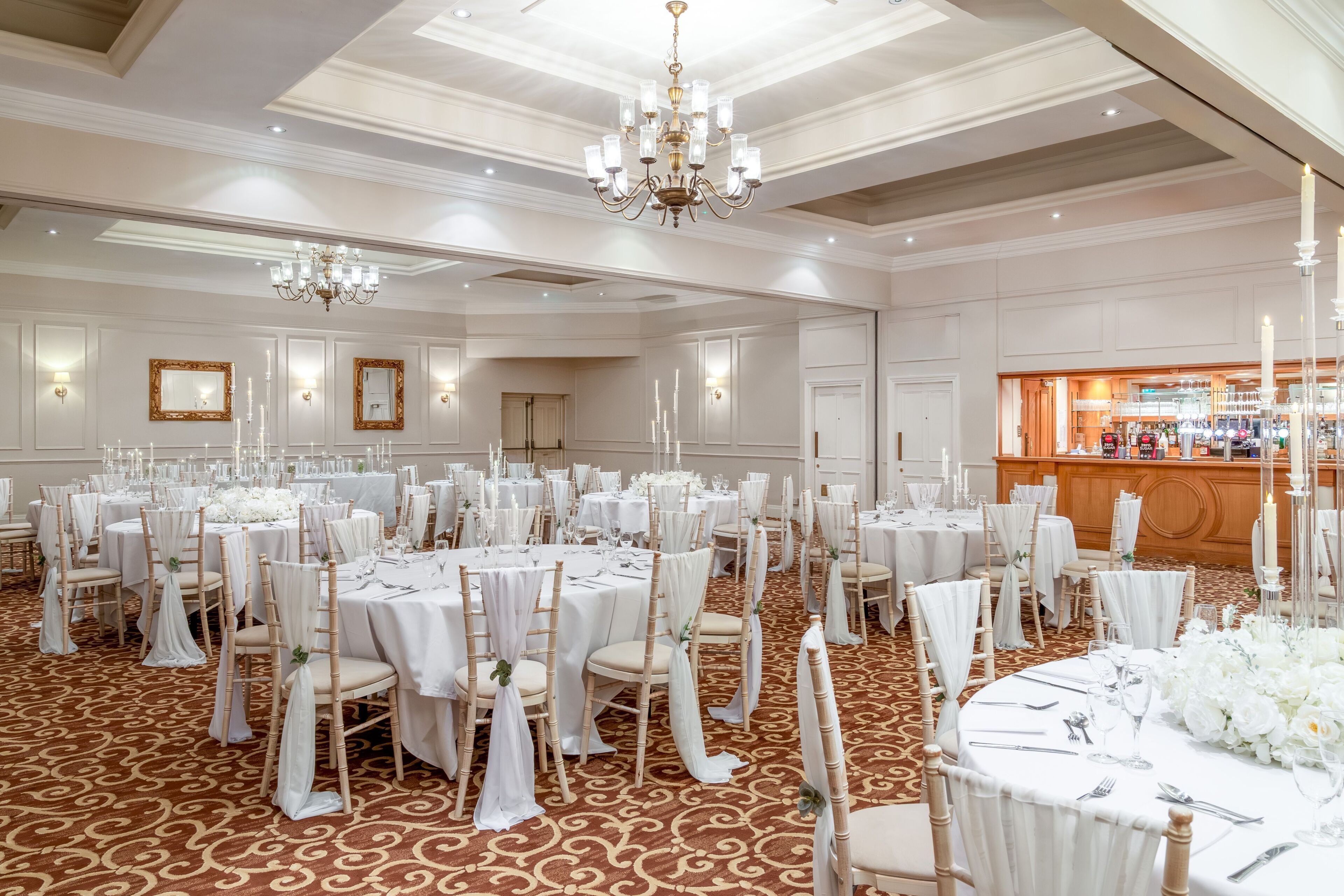 Een feestzaal met ronde tafels, witte tafelkleden en kroonluchters.
