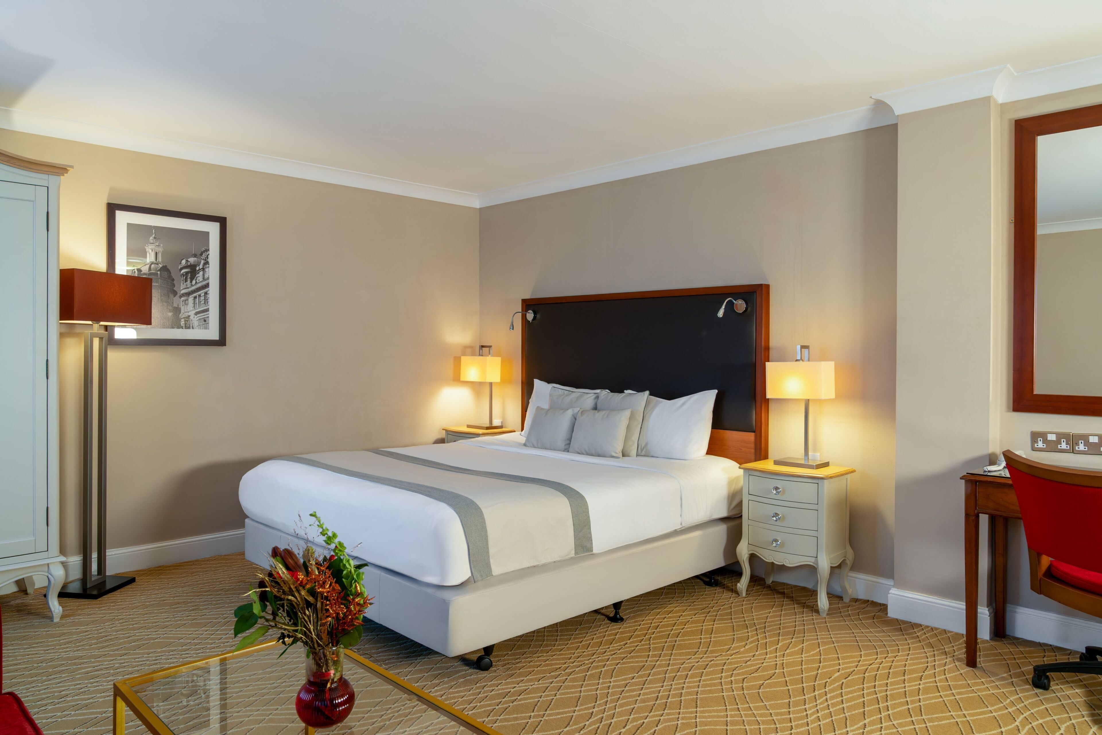 A hotel room with a large bed, bedside tables, a desk, and a mirror.