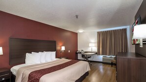 Quarto de hotel com uma cama grande, uma mesa de trabalho, uma cadeira, luminária de mesa, TV de tela plana e janela com cortinas.