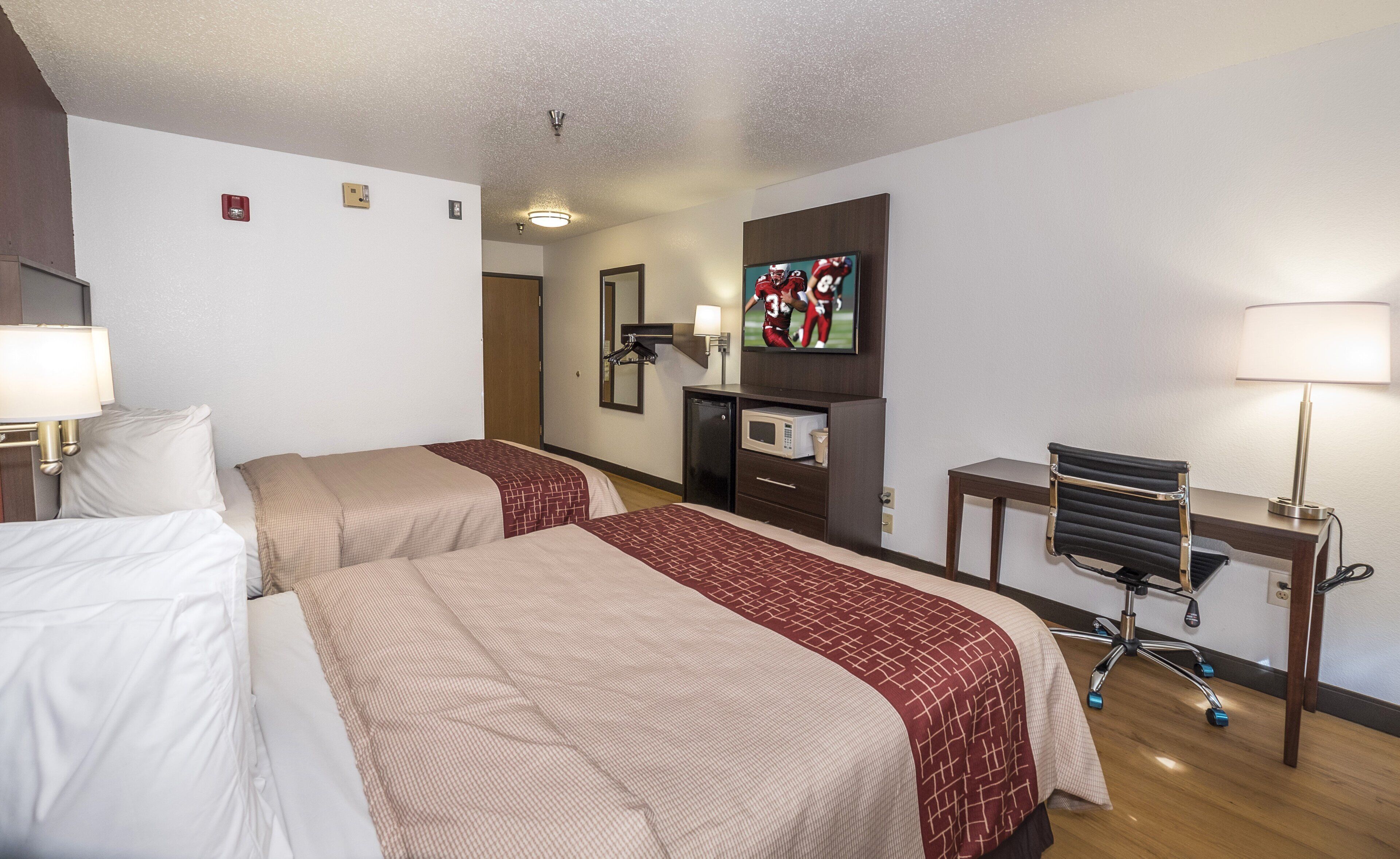 Habitación de hotel con dos camas, un escritorio, una silla, un televisor y un microondas.