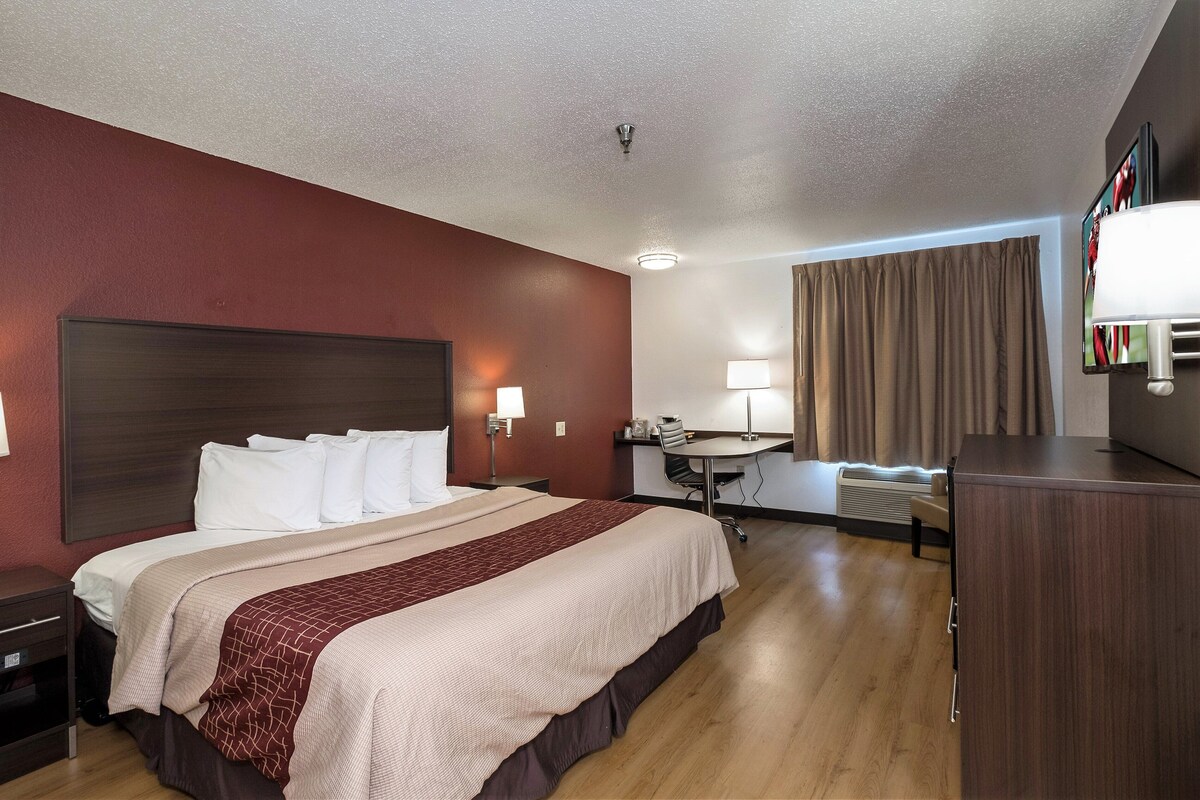Une chambre d’hôtel avec un grand lit, des tables de chevet, un bureau, une chaise, une télévision et une fenêtre avec des rideaux.