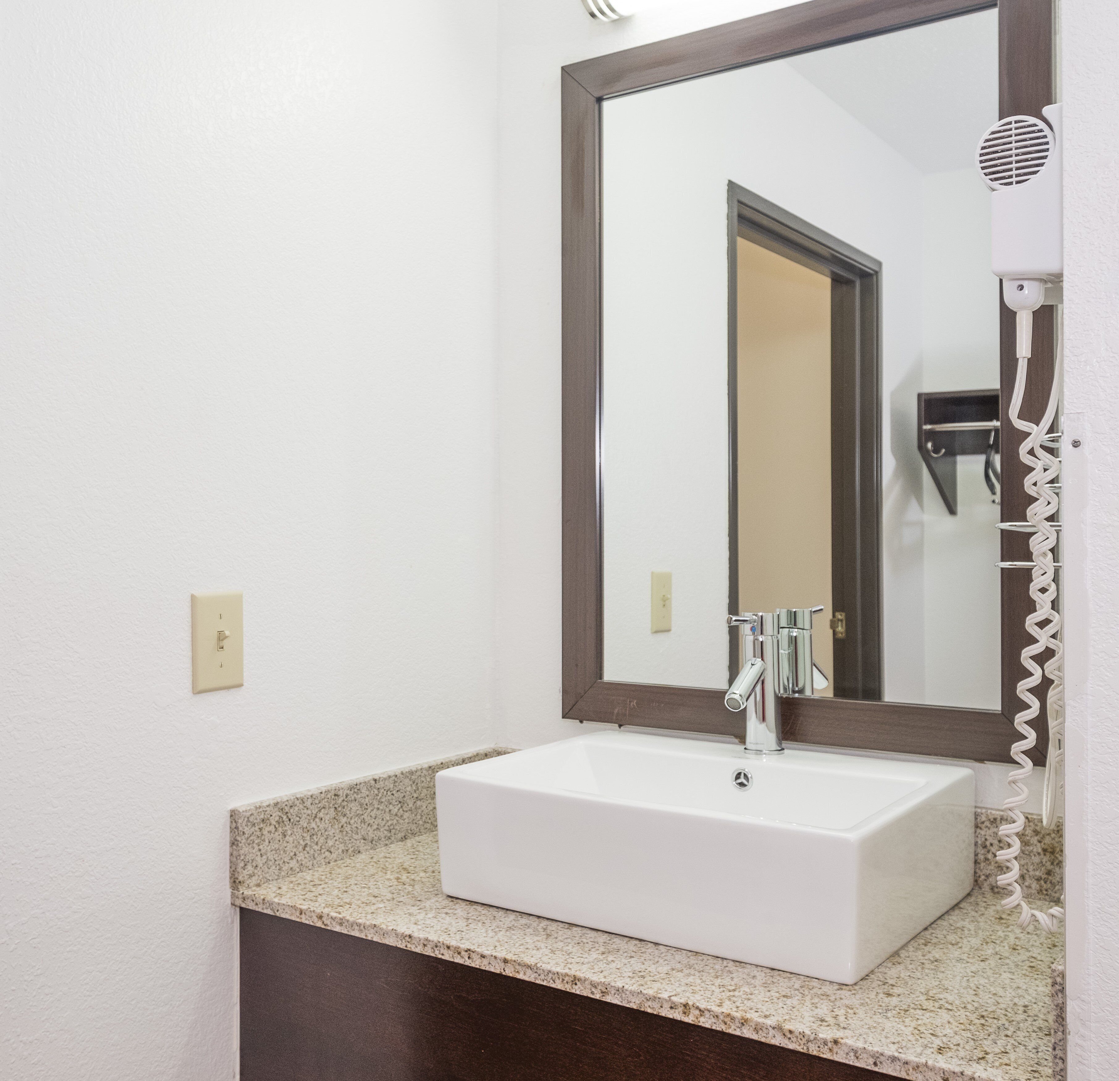 A bathroom with a white sink, a mirror, and a hairdryer on the wall.