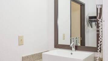 A bathroom with a white sink, a mirror, and a hairdryer on the wall.