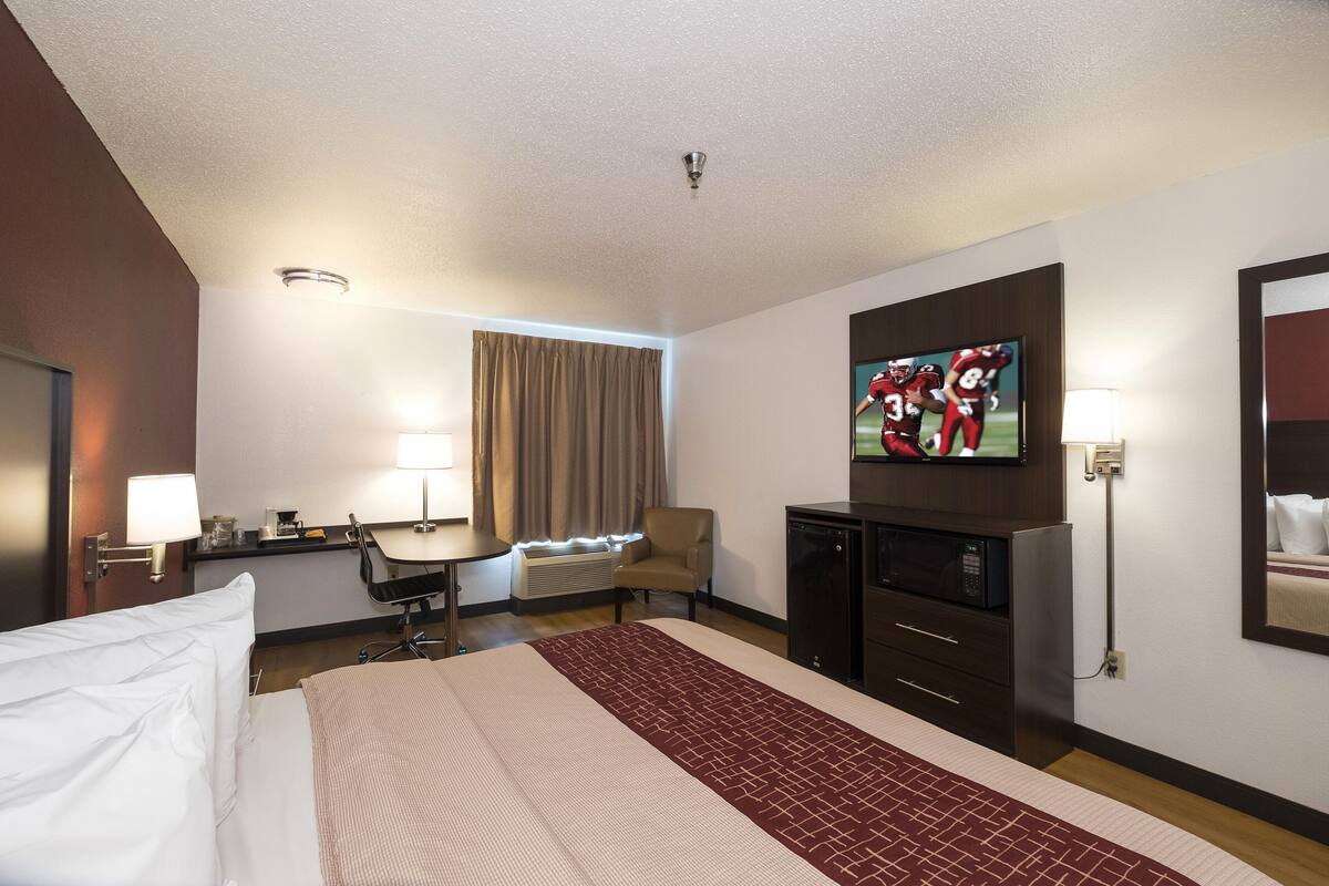A hotel room with a bed, desk, chair, television, and a minibar.