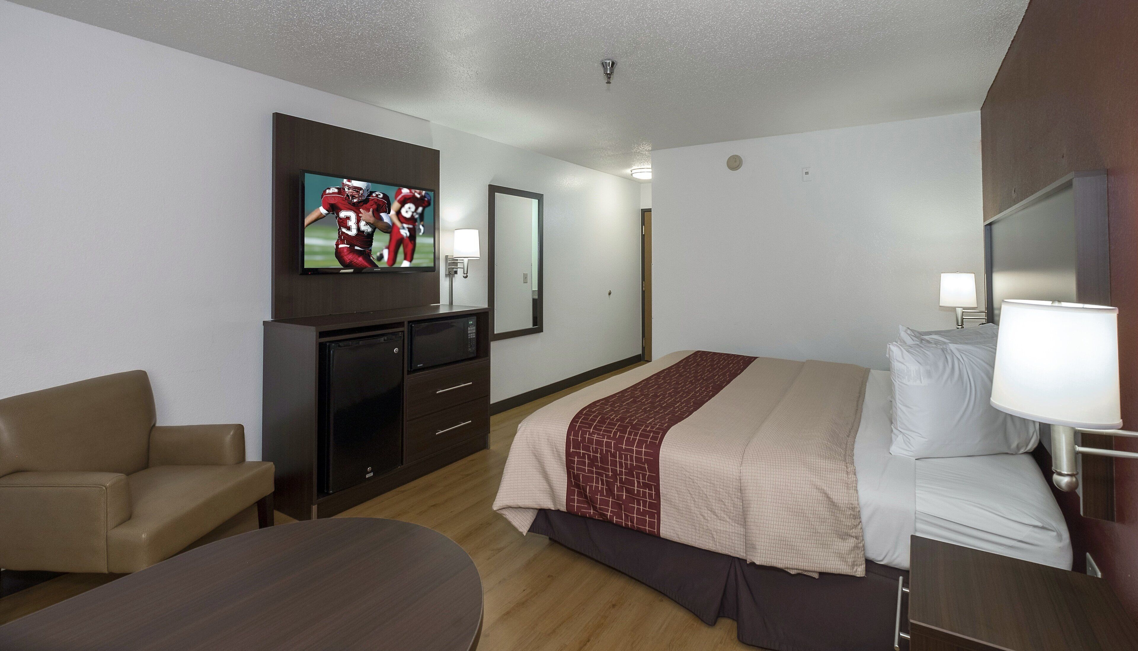A hotel room with a bed, a TV, a desk, a chair, and a bedside table.