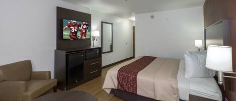 A hotel room with a bed, a TV, a desk, a chair, and a bedside table.