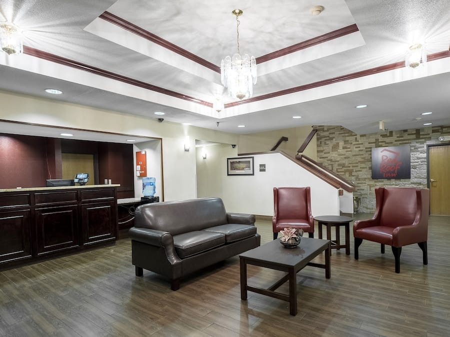 Un hall de hotel con mostrador de recepción, un sofá de cuero, dos sillones, una mesita y una escalera que sube a otro piso.