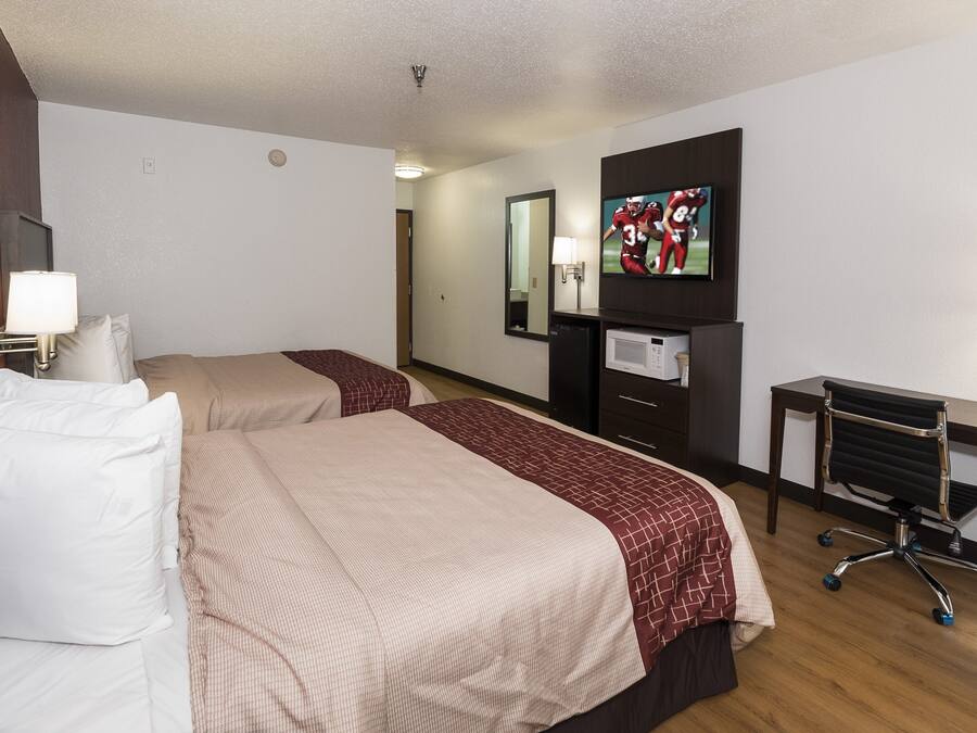 A hotel room with two beds, a desk with a chair, a television, and a mirror.