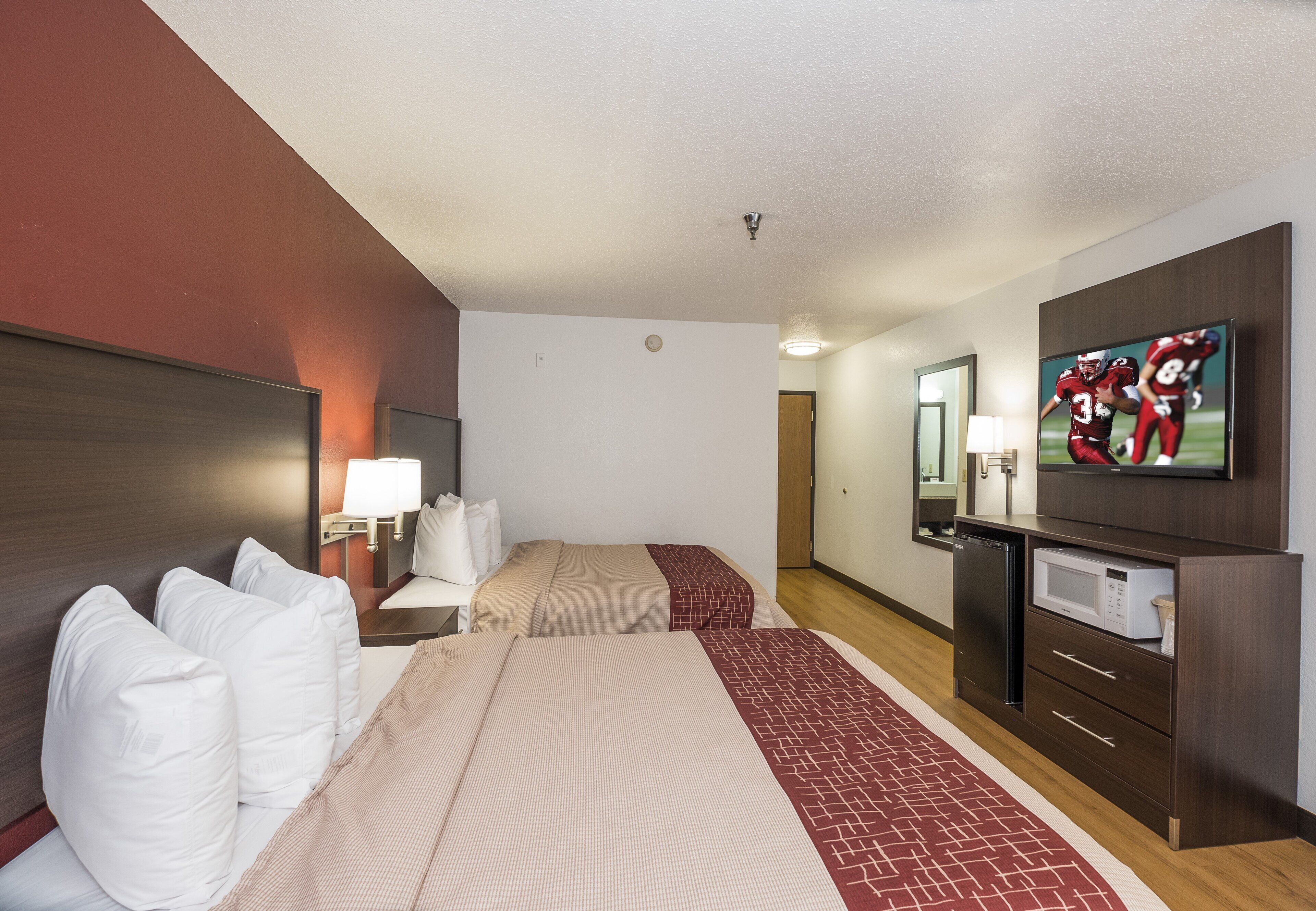 Habitación de hotel con dos camas, televisión, microondas y un refrigerador pequeño.