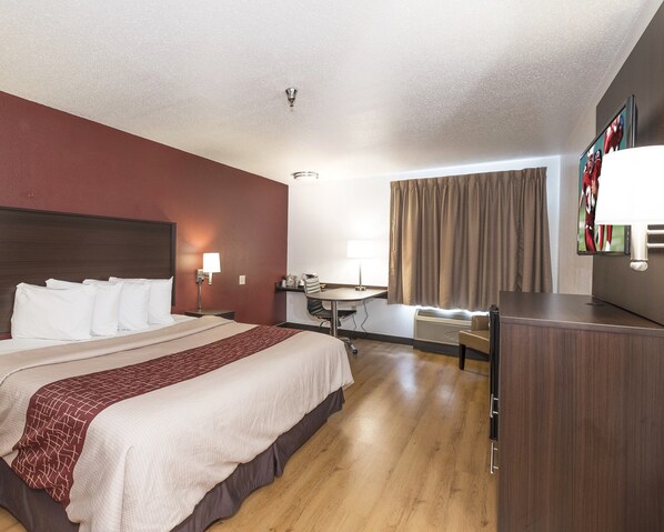 A hotel room with a large bed, a desk, a chair, and a TV.