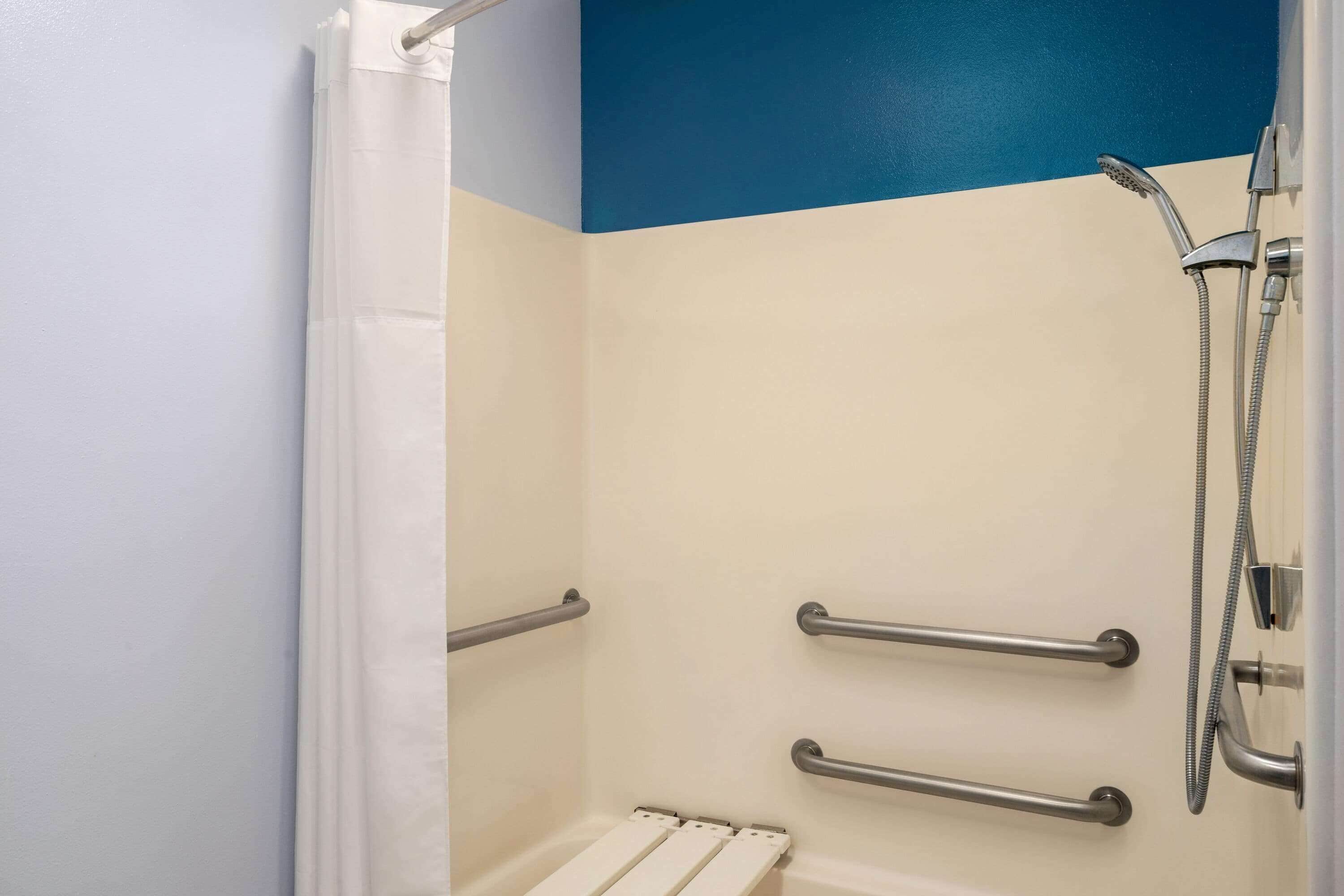 Una doccia con tenda bianca, parete blu e soffione a mano.