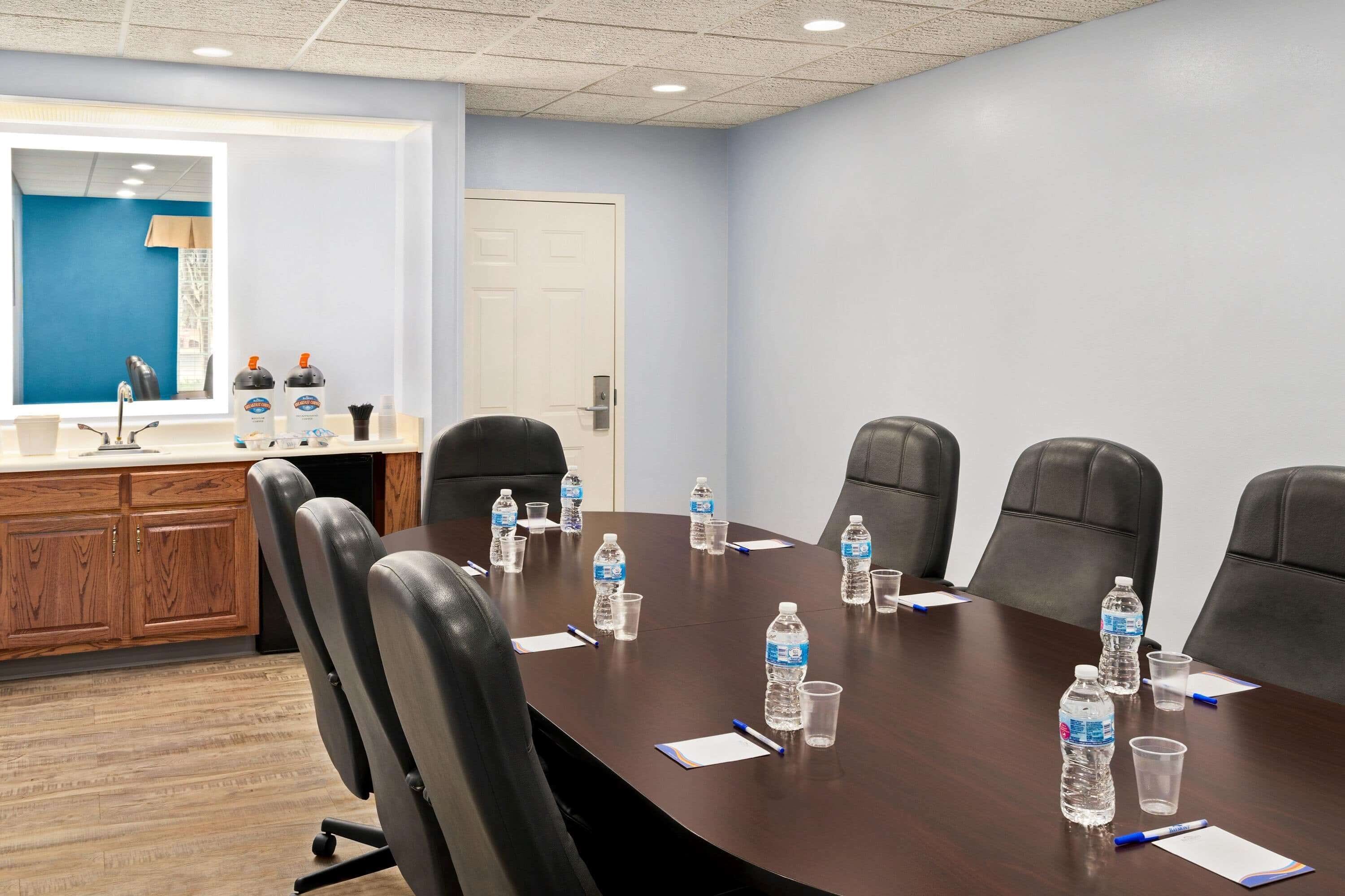 A conference room with a long table, six chairs, water bottles, and notepads.