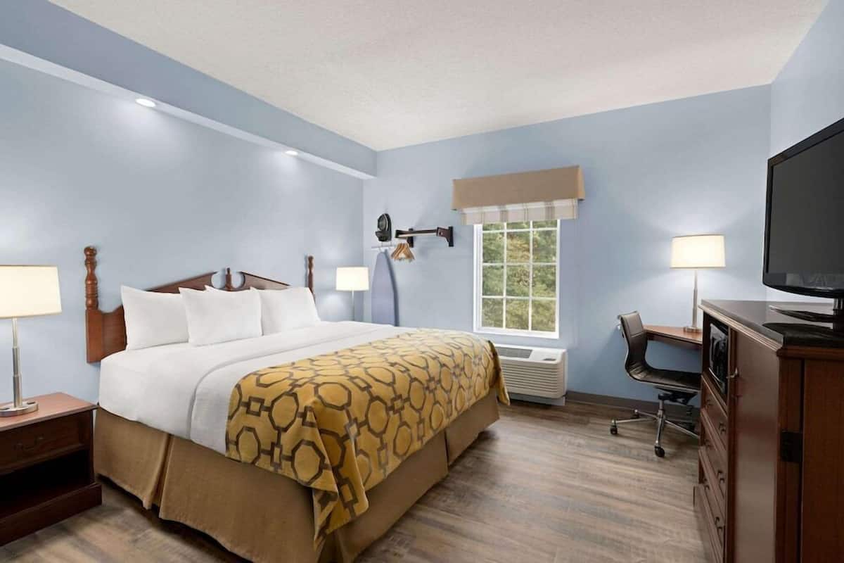 Quarto de hotel com cama, luminárias de cabeceira, escrivaninha com cadeira, televisão e janela com persianas.