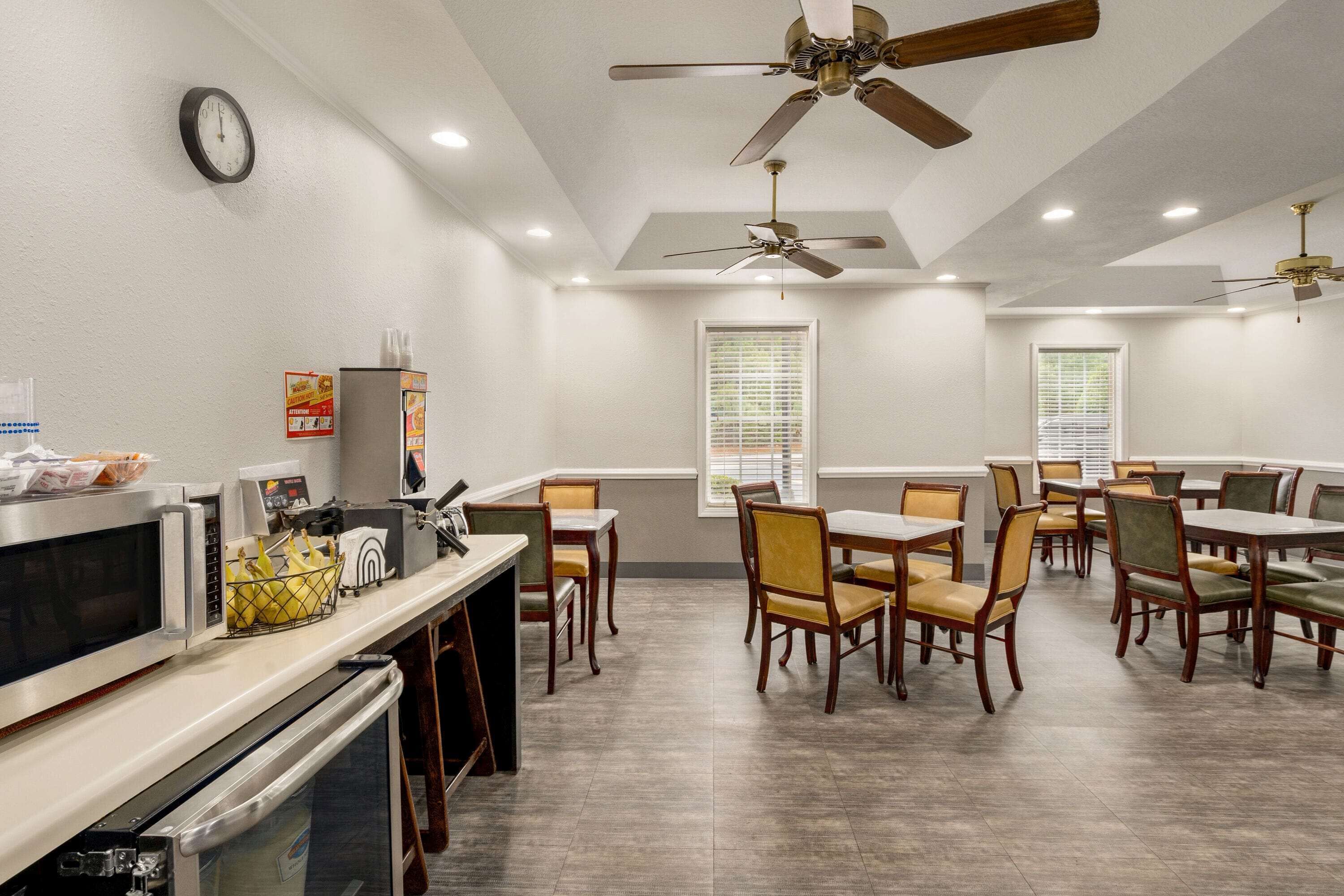 A dining area with tables and chairs, ceiling fans, a clock, and a microwave.