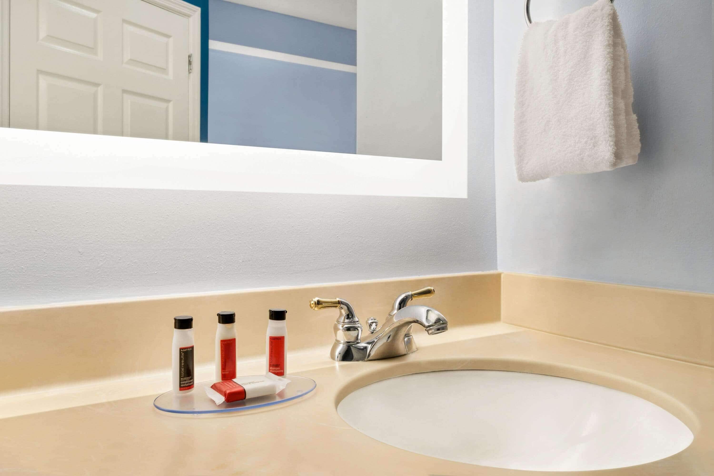 A bathroom with a white sink, a mirror, and a towel hanging on the wall.
