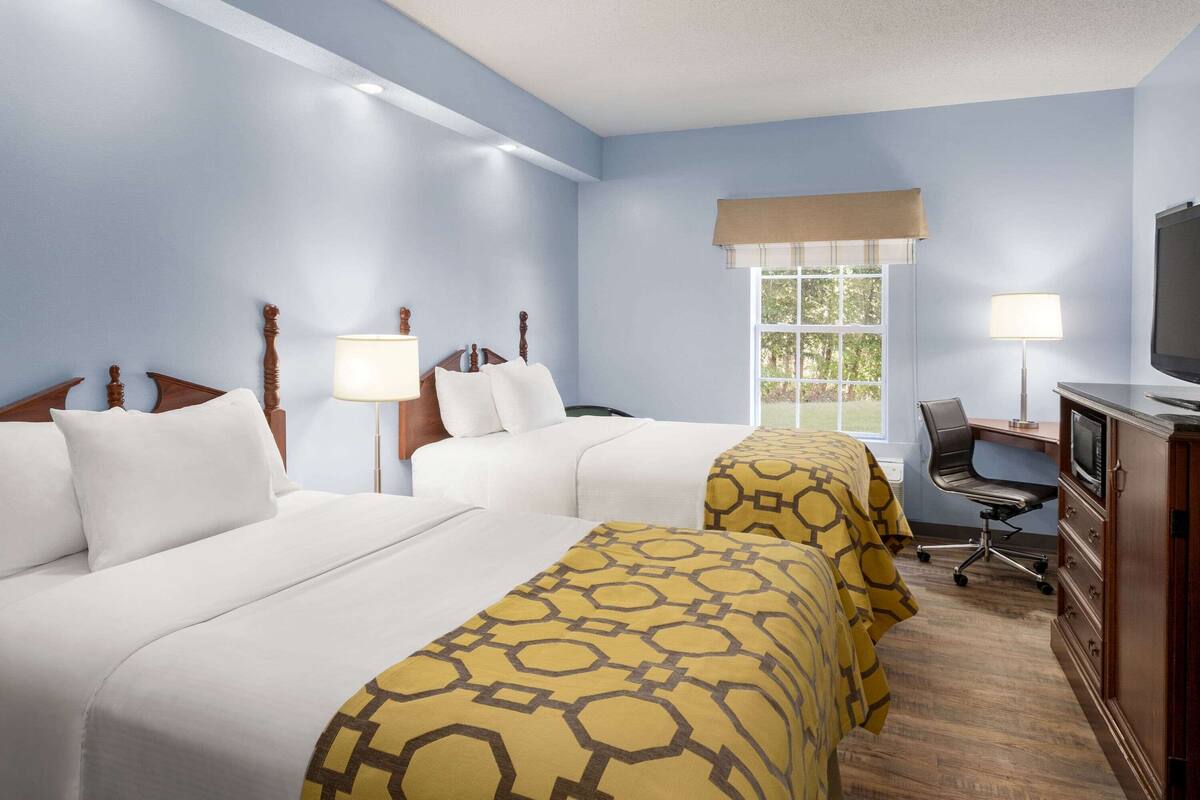 Quarto de hotel com duas camas, uma escrivaninha, televisão e janela com vista para áreas verdes.