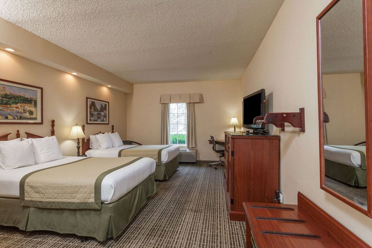 Habitación de hotel con dos camas, un escritorio, un televisor y un espejo grande.